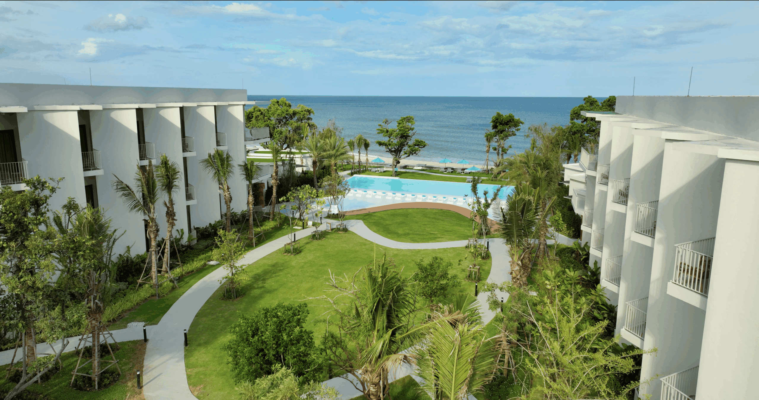 Luxurious beachfront resort at Aviyana Hua Hin Hotel with modern white buildings, lush greenery, and a pristine infinity pool overlooking the ocean. Perfect for relaxation and luxury vacationin.